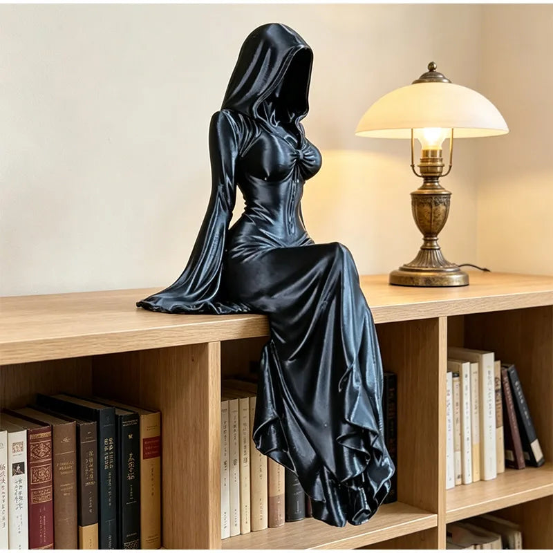 A black satin-like figure draped in a hooded cloak is seated on a wooden shelf next to a lamp.