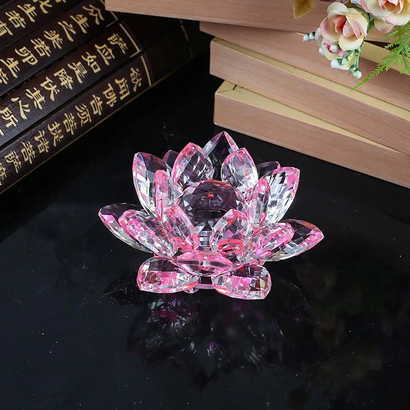 A pink crystal lotus flower ornament resting on a dark surface next to stacked books.