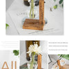 A clear glass vase holds a white flower in a wooden stand on a white background.