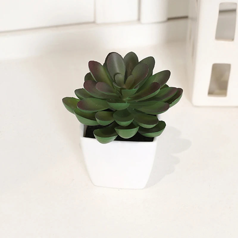A small, dark green artificial succulent plant in a white pot sitting on a light surface.