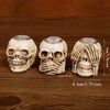 Three resin skull candle holders in off-white color displayed on a wooden surface.