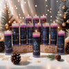 A collection of dark purple glass candles featuring zodiac signs, set against a soft, festive background with pine branches a