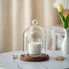 A glass aromatherapy candle holder with a white candle on a wooden base and dust-proof cover.