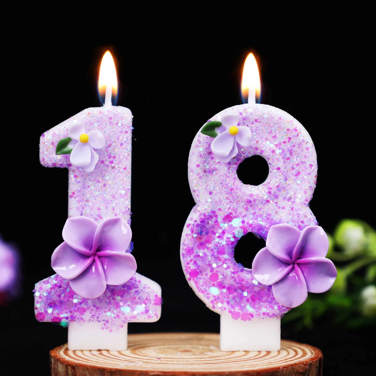 Two glitter flower number candles, 1 and 8, are lit against a black background.