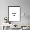 A framed canvas art print with the text NEVER GIVE UP on a white background, displayed on a wooden table.