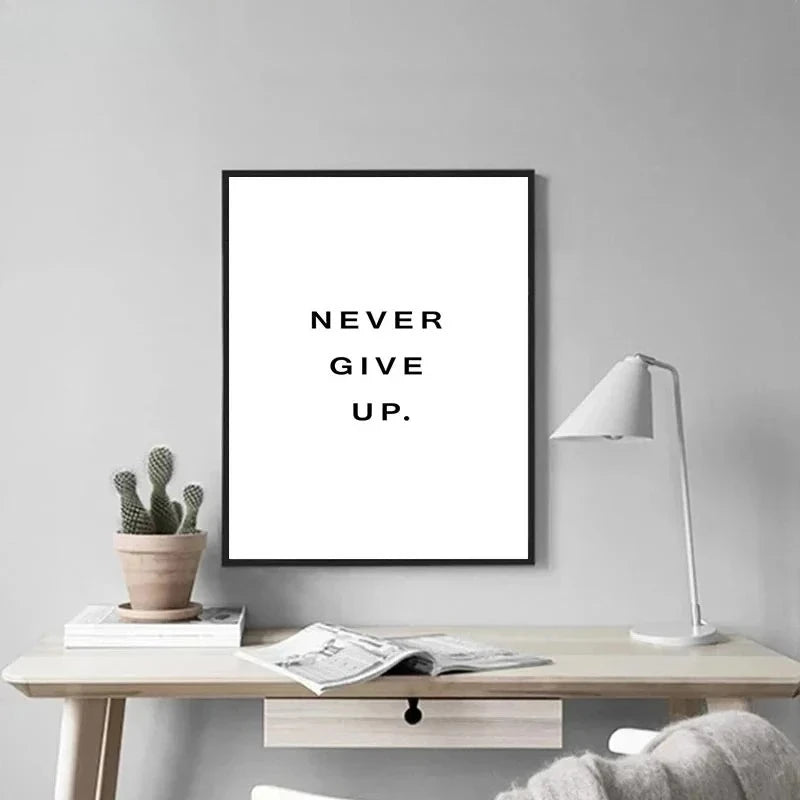 A framed canvas art print with the text NEVER GIVE UP on a white background, displayed on a wooden table.