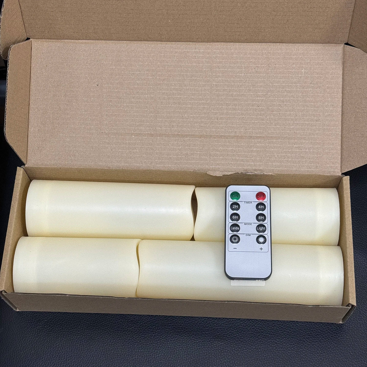 A cardboard box containing four white flameless LED candles and a remote control.