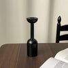 A black vintage wooden candle holder with a flared top and cylindrical base sits on a dark wooden table.