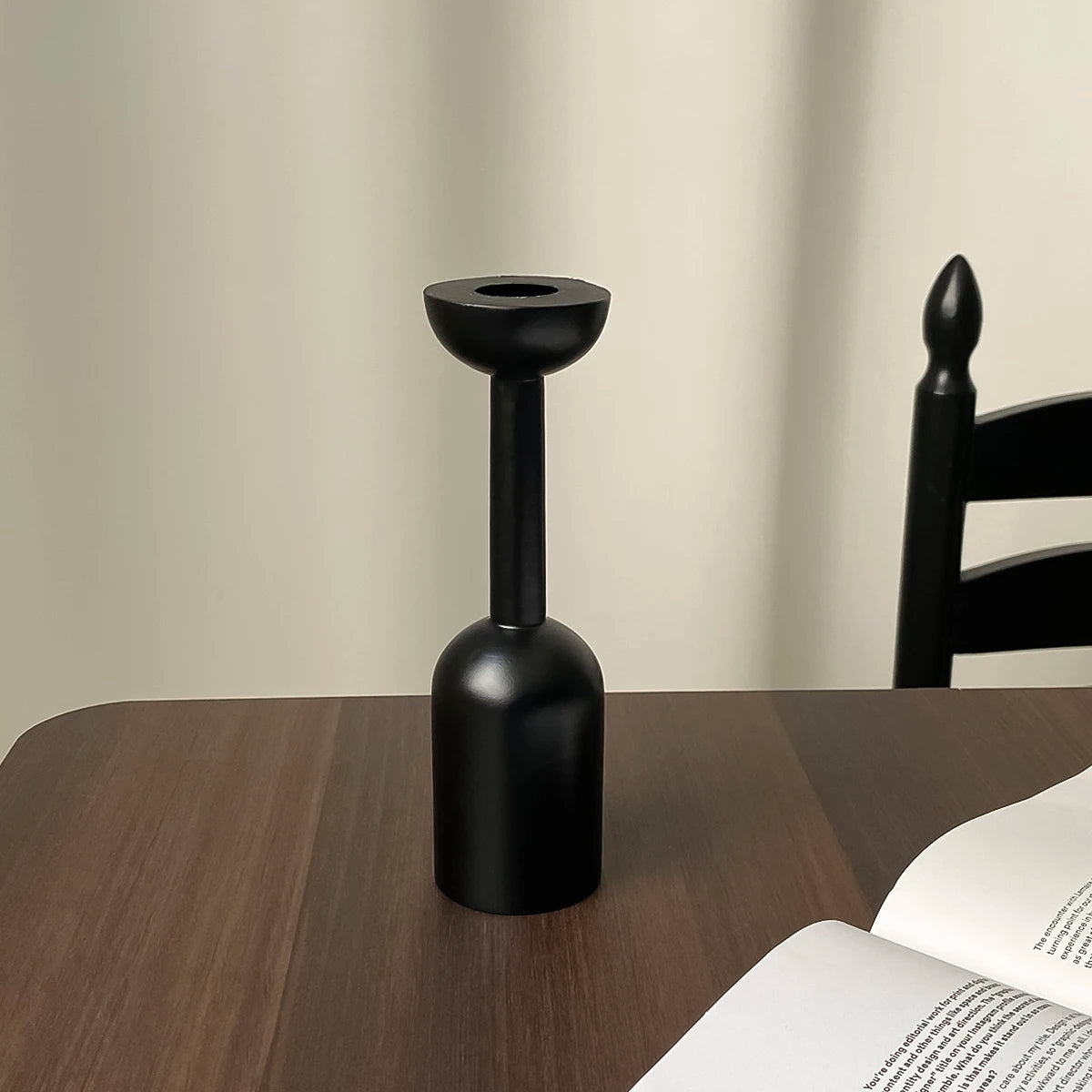 A black vintage wooden candle holder with a flared top and cylindrical base sits on a dark wooden table.