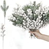 A hand holds a bouquet of frosted pine needles and white berries for a Christmas arrangement.