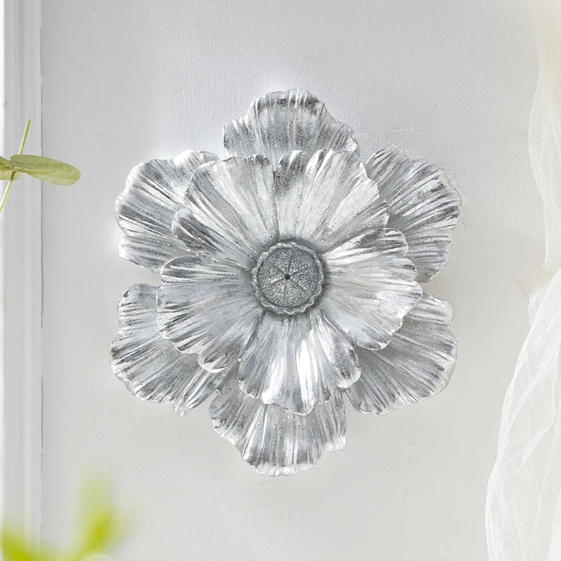 Silver resin flower wall art with layered petals mounted on a white wall.