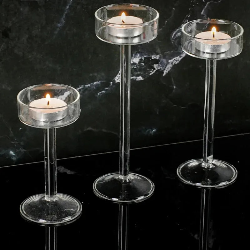 Three clear crystal glass candle holders with lit candles displayed on a black marble surface.