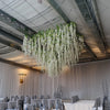 A long, cascading garland of white silk wisteria vines hangs from the ceiling in a modern interior setting.