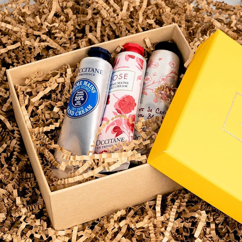 Drei Flaschen Occitane Rose Eau de Cologne in einer Kartonbox mit zerknülltem Papierfüllmaterial.