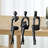 Three black abstract thinker sculptures made of resin displayed on a wooden desk.