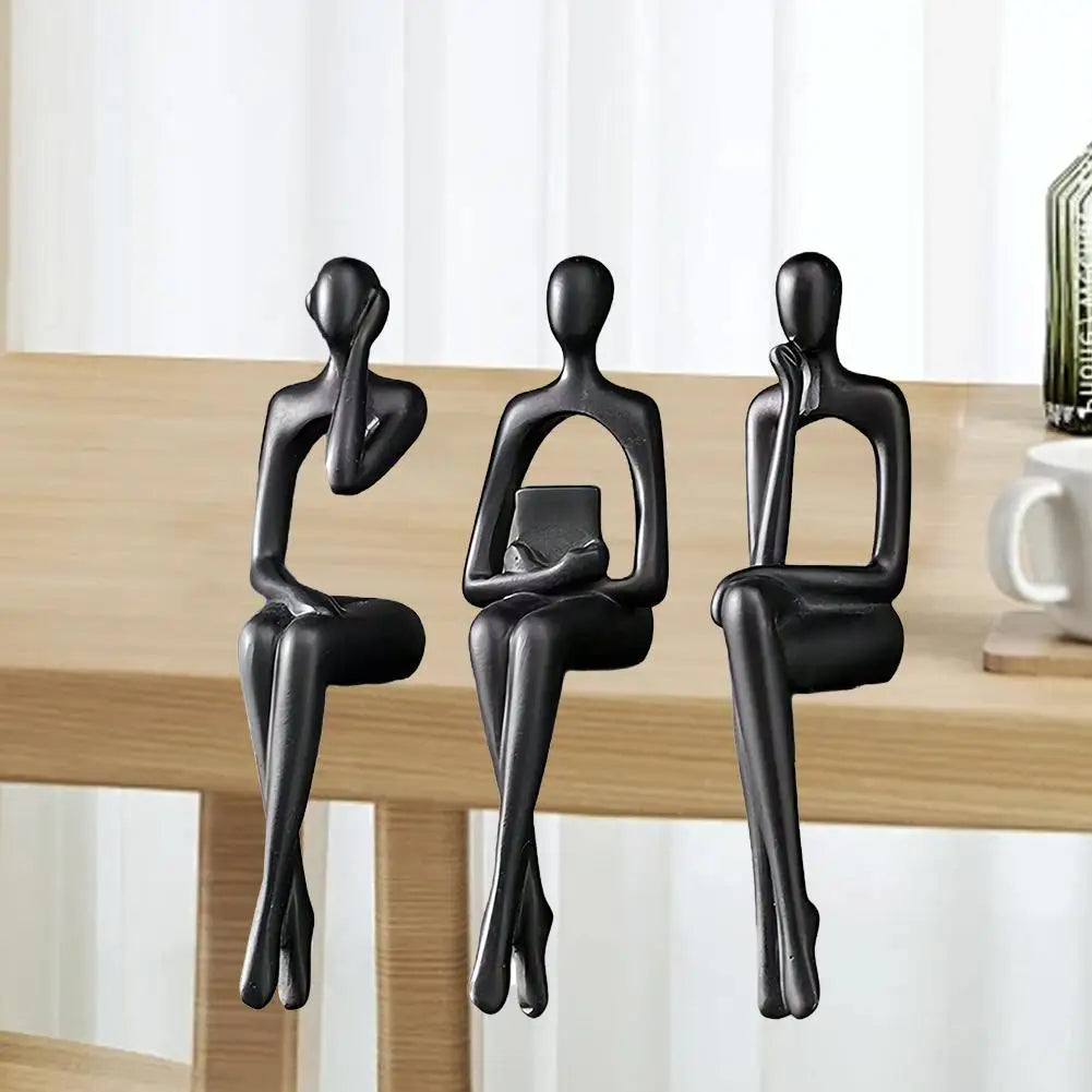 Three black abstract thinker sculptures made of resin displayed on a wooden desk.