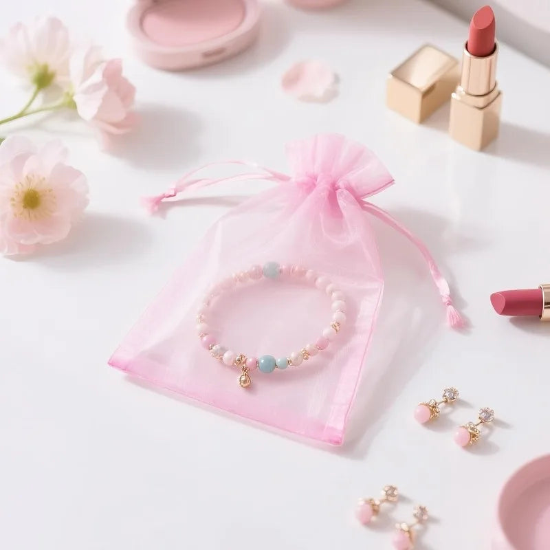 Pink organza drawstring bag with a pearl bracelet and gold lip product displayed on a white surface.