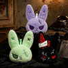 A purple bunny plush keychain with purple ears and a green bunny plush with green ears.