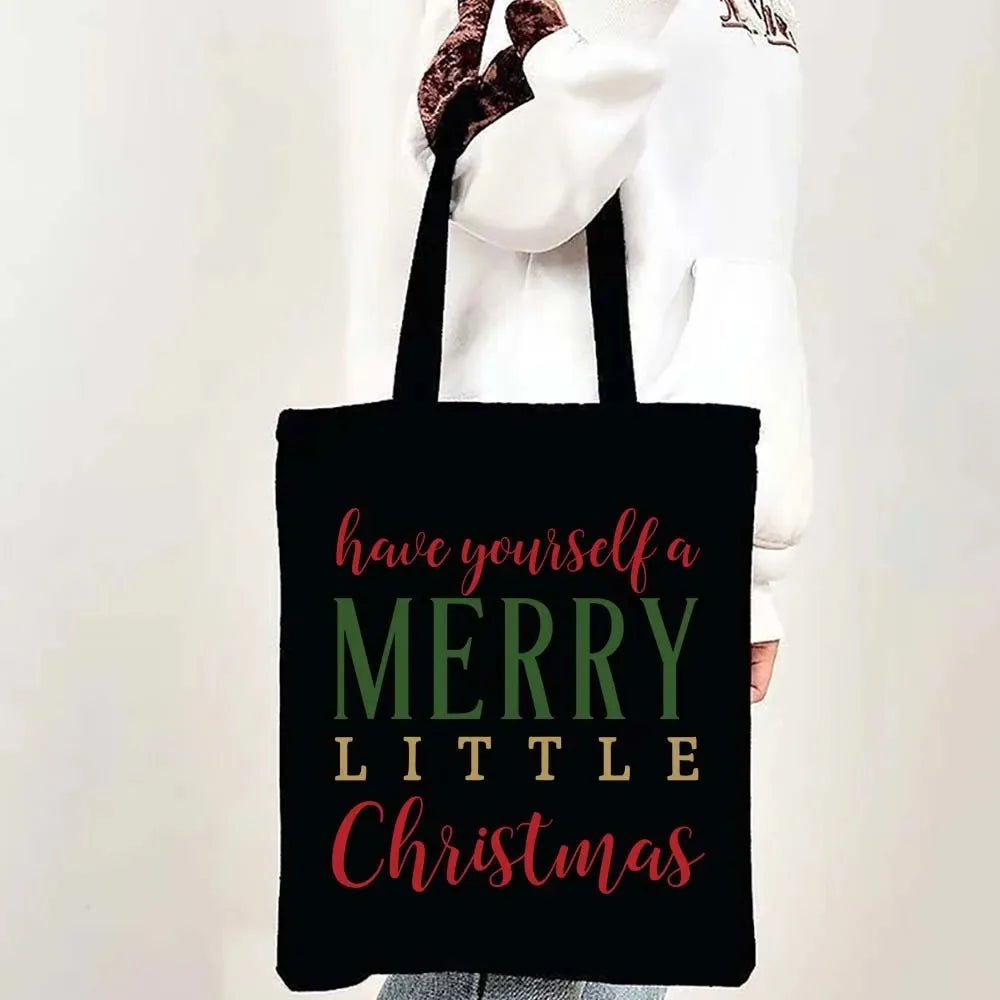 A black tote bag with pink and green text that reads Have yourself a Merry Little Christmas