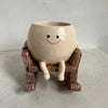 A ceramic ornament shaped like a smiling face sitting on a wooden plank.
