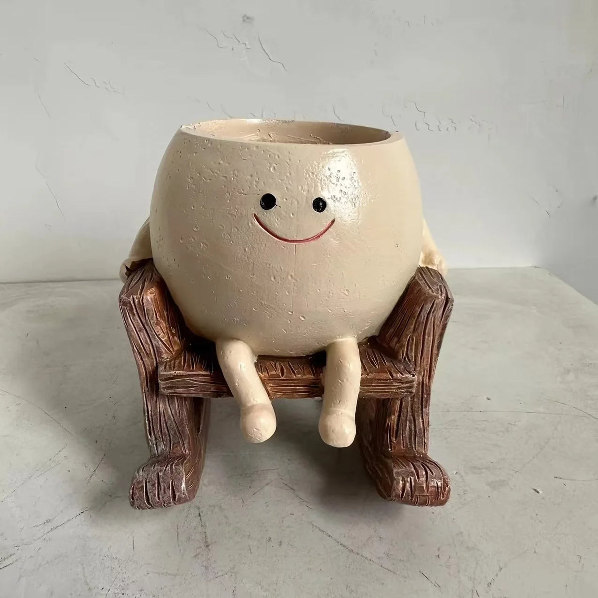A ceramic ornament shaped like a smiling face sitting on a wooden plank.
