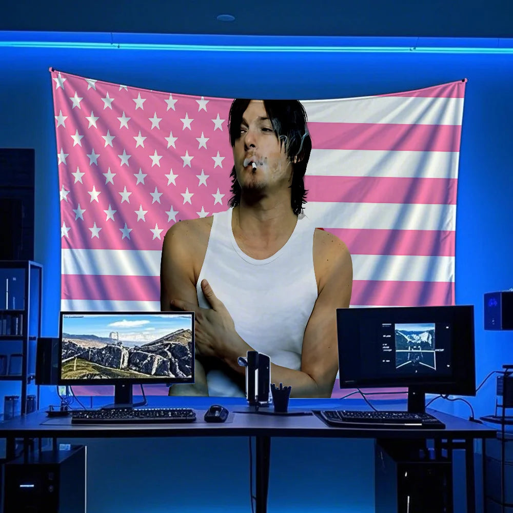 A man sits in front of a large American flag banner decorated with pink and white stripes and stars, with computer monitors v