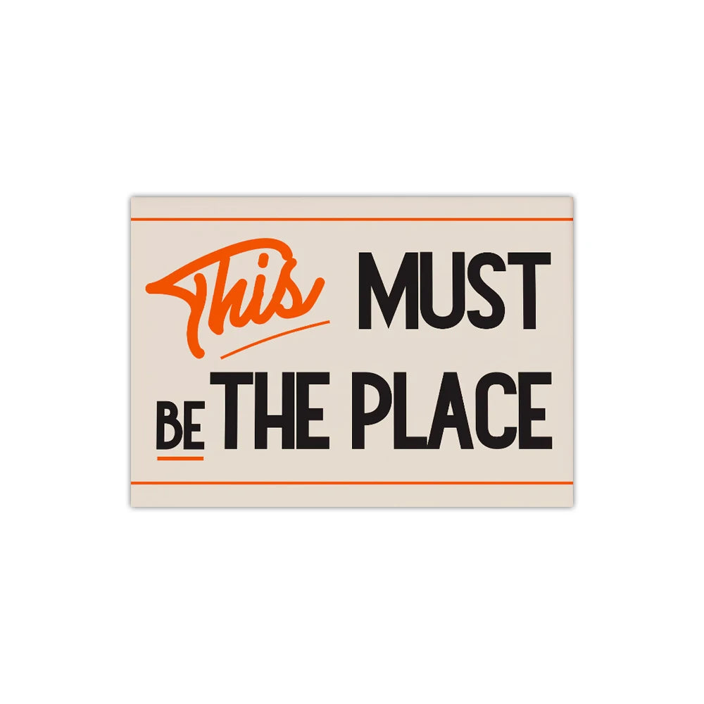 Wall art featuring the text This Must Be The Place in orange and black typography on a beige background