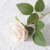 A soft pink artificial rose with green leaves on a white textured background.