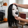 A person is applying white latex makeup to a face while it is styled with long black hair.