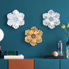 A display of large flower-shaped resin wall art in white and gold tones against a dark teal wall.