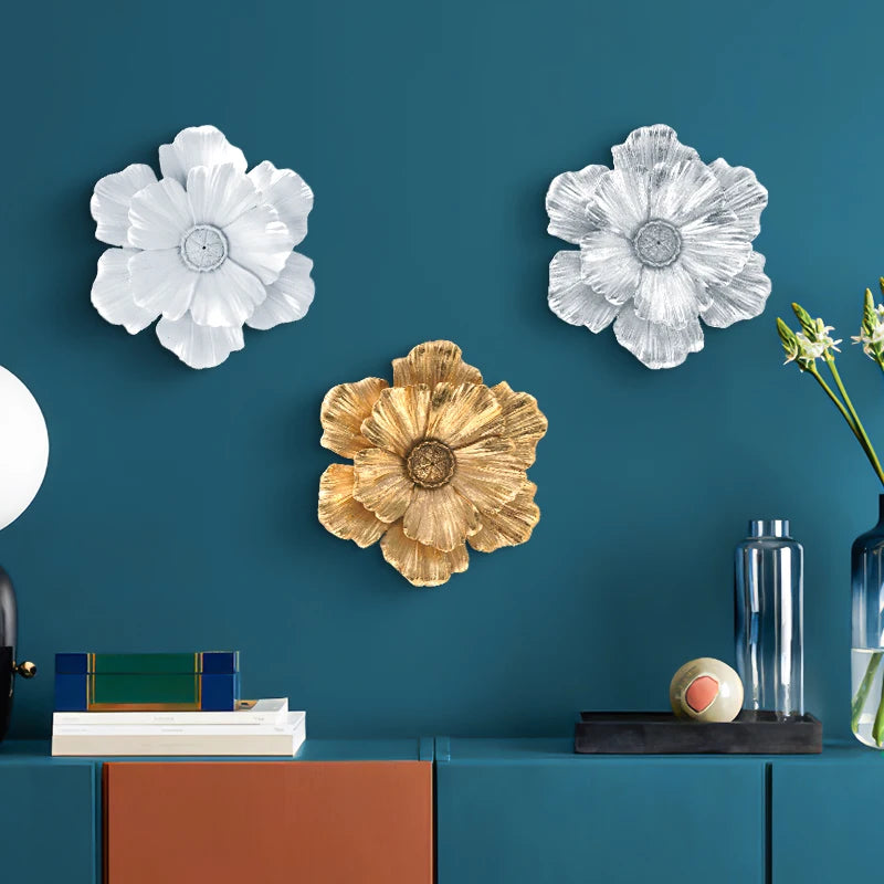 A display of large flower-shaped resin wall art in white and gold tones against a dark teal wall.
