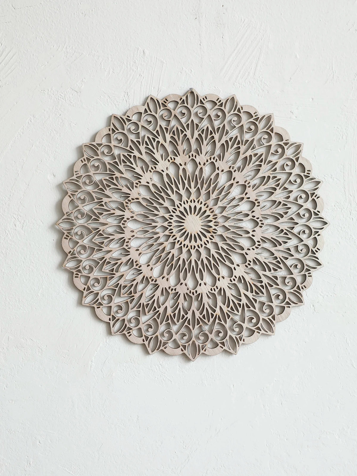 Decoración de pared tipo mandala de madera clara con intrincados patrones recortados montada en una pared blanca.