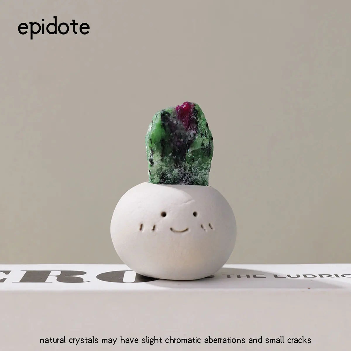 A small, bean-shaped decorative stone with a green and purple crystal inclusion sits on a white surface.