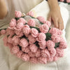 A handmade rose bouquet blanket gift made of pink and green yarn is resting on a white fabric.