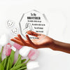 A hand holds a hexagonal acrylic plaque engraved with 'To My Brother' and a fist bump design, surrounded by pink and white tu