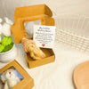 A small cardboard box containing a yellow teddy bear plush and an encouraging note on a white background.
