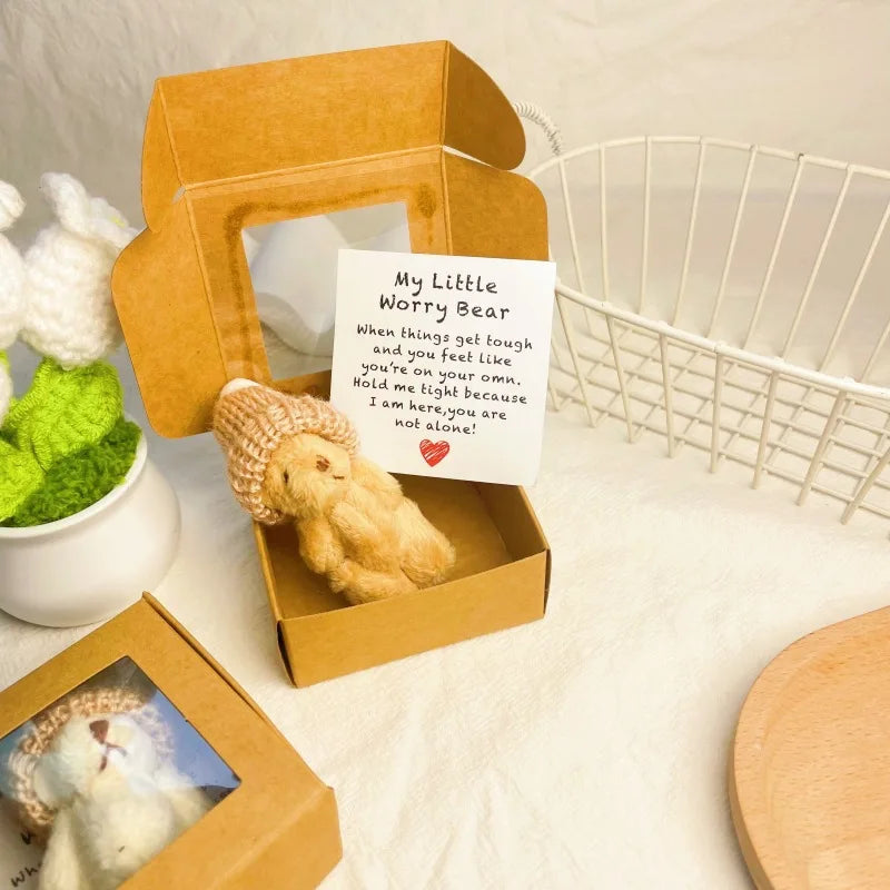 A small cardboard box containing a yellow teddy bear plush and an encouraging note on a white background.