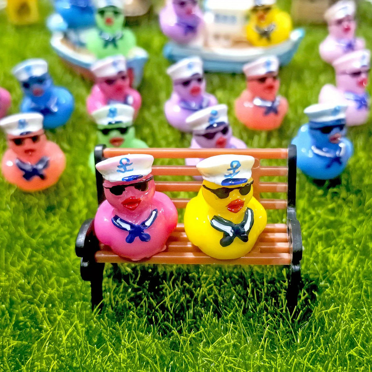 A collection of mini resin cruise ducks with sunglasses in various colors sitting on green grass.