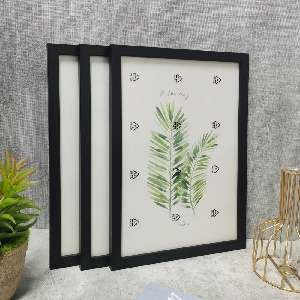 A set of three black wooden photo frames with white mats displaying a green palm leaf illustration.