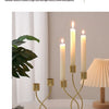 A set of tall, slender iron candlesticks with white wax candles displayed on a light-colored table.