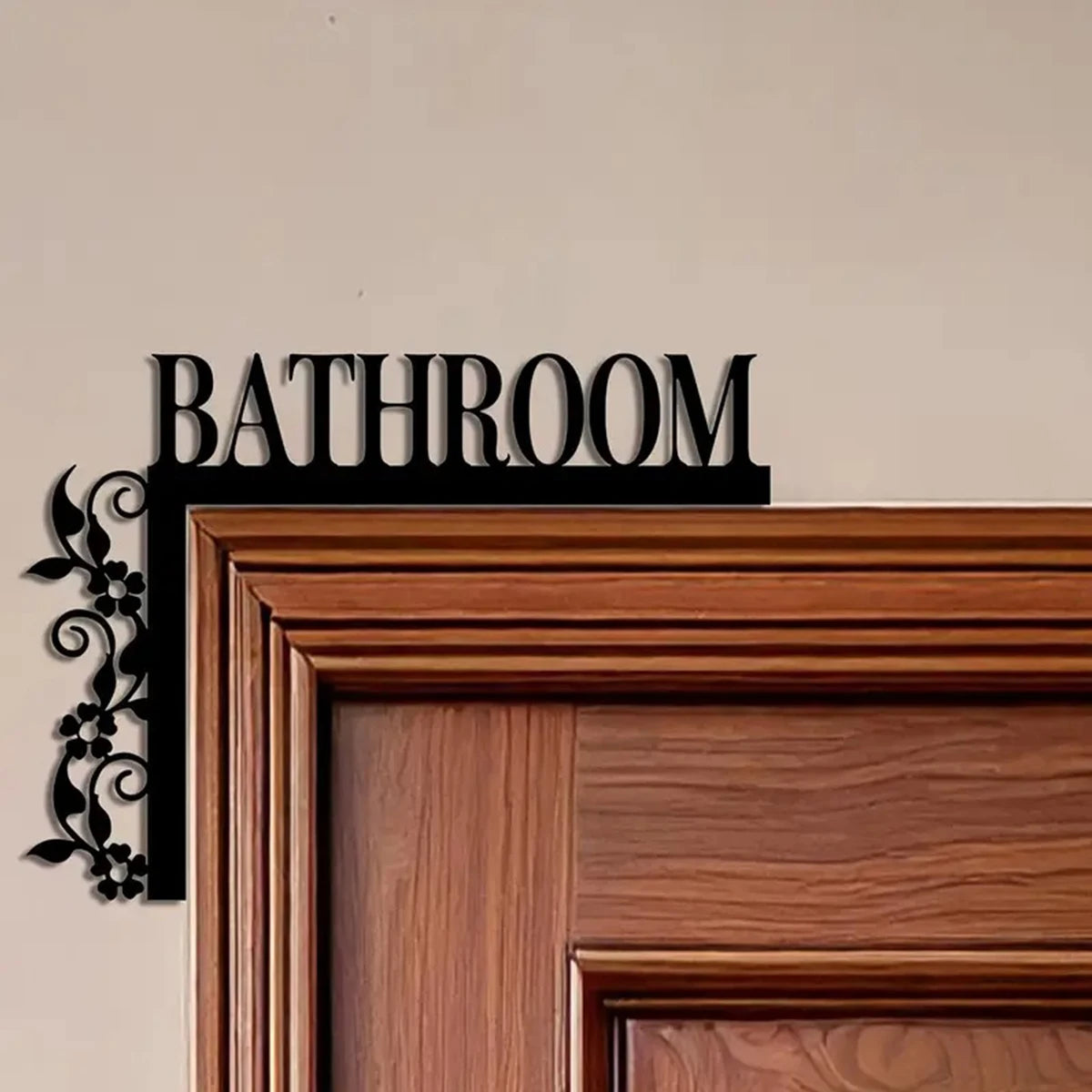 A dark metal bathroom sign with the word BATHROOM mounted on a wooden door frame.