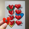 A set of heart-shaped fridge magnets in red and blue colors arranged on a white board.