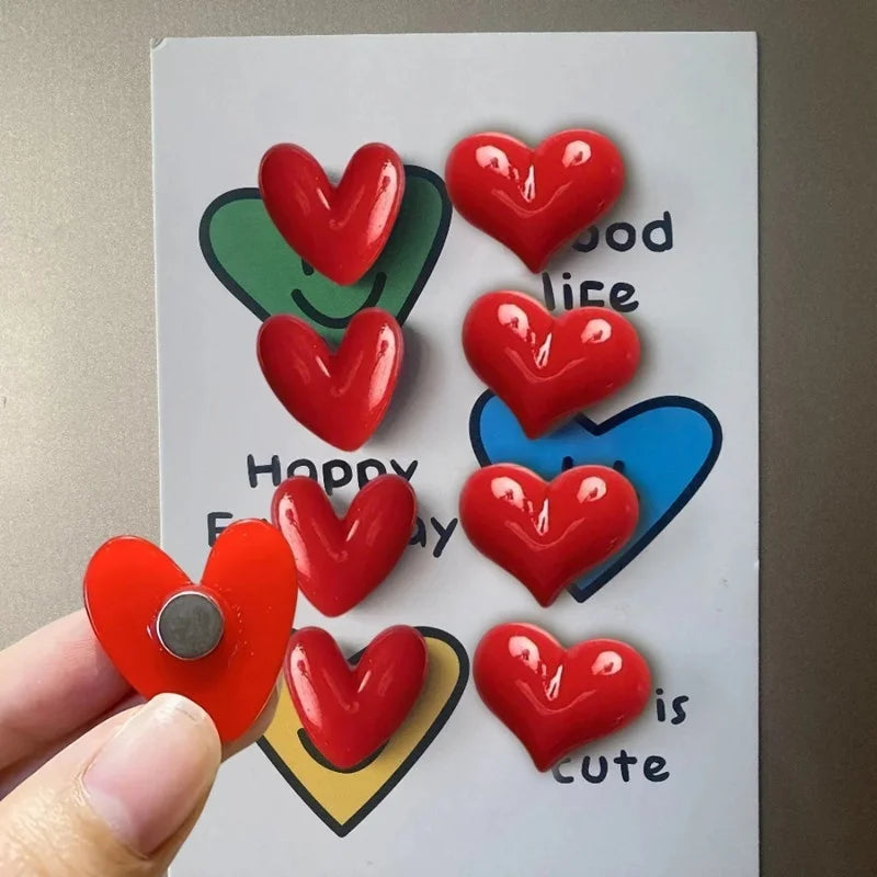 A set of heart-shaped fridge magnets in red and blue colors arranged on a white board.