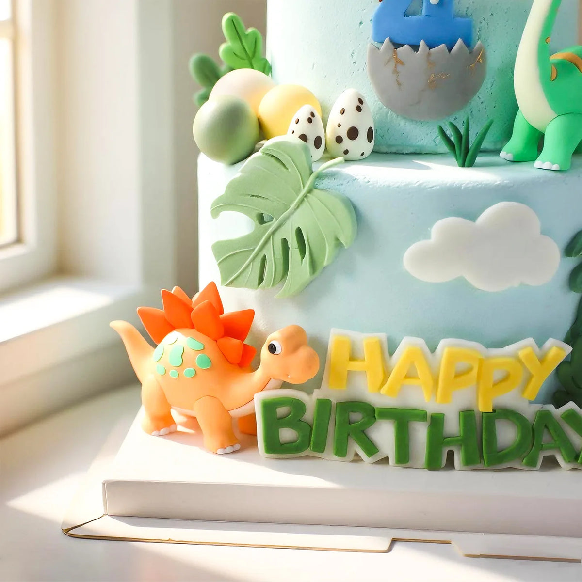 Pastel de varios pisos decorado con elementos de dinosaurios verdes y amarillos, incluyendo una gran hoja de planta y un letr