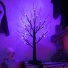 A dark silhouette of a birch tree with glowing LED lights against a purple background.