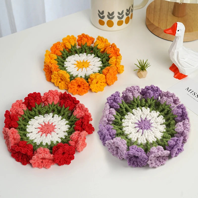 Three hand-crocheted rose flower coasters in orange, red, and purple displayed on a white surface.
