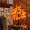 Arbre de bouleau noir artificiel avec des lumières LED orange vif, sur une table en bois près d'une cheminée en pierre.