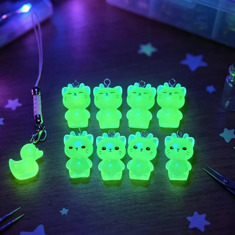 A collection of glow-in-the-dark cartoon kitty charms in various sizes and expressions displayed on a dark surface.