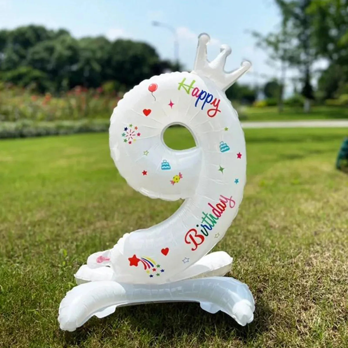 A white foil balloon shaped like the number 9 with a crown and birthday text standing on the grass.