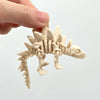 A hand holds a light beige 3D printed dinosaur skeleton model for desktop display.